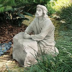 a statue of a man sitting on top of a rock in the middle of a garden