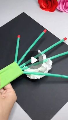 someone is cutting out paper with scissors on top of a piece of black paper that has red and green sticks sticking out of it