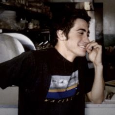 a young man talking on a cell phone in front of a kitchen counter and shelves