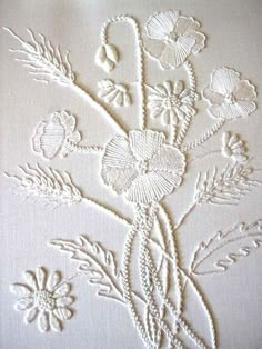 an embroidered piece with flowers and leaves on white linen, in the shape of a cross stitch