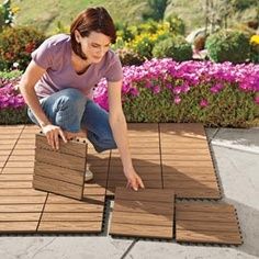 a woman kneeling down on top of a wooden floor next to purple flowers and plants