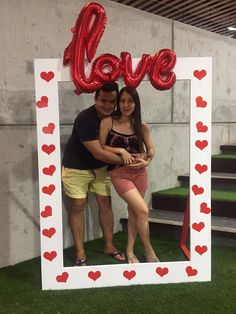 a man and woman standing in front of a photo frame with the word love on it