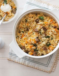 two bowls filled with rice and vegetables on top of a white table next to a spoon