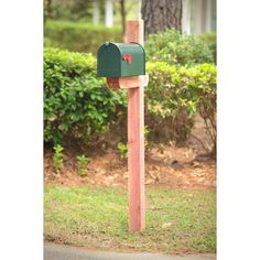 a green mailbox sitting on top of a wooden post in front of some bushes