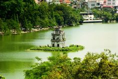 an old tower in the middle of a lake surrounded by trees and buildings on both sides