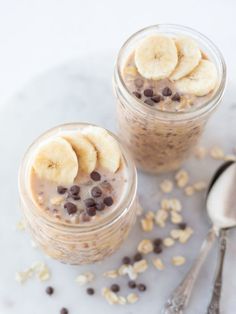 two jars filled with oatmeal and bananas on top of a white table