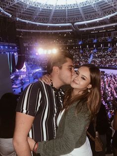 a man and woman are kissing in front of an arena full of people at a concert