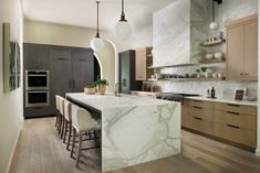 a large kitchen with marble counter tops and wooden cabinets in the center, surrounded by hanging lights