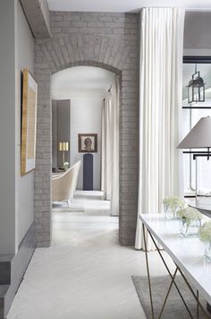 a hallway with white walls and flooring next to a table in front of a window