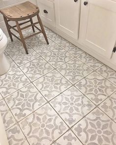 a white toilet sitting next to a wooden chair in a bathroom on top of a tiled floor