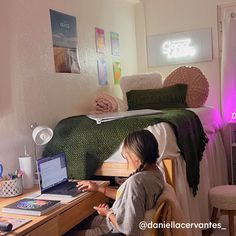 a woman sitting in front of a laptop computer on top of a desk next to a bed