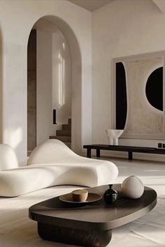 a modern living room with white furniture and black accessories on the coffee table in front of an arched doorway