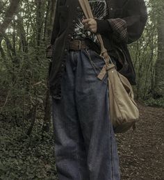 a person standing in the woods with an umbrella and bag on his shoulder, holding a cane