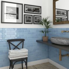 a bathroom with blue tiles and pictures on the wall above the sink, along with a chair