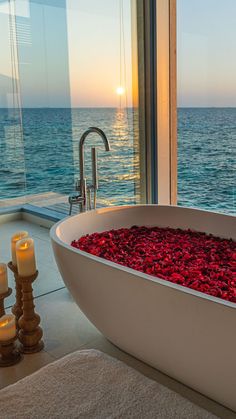 a bathtub filled with red flowers next to candles on a counter top near the ocean