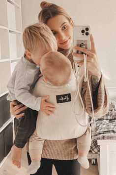 a woman holding a baby taking a selfie with her cell phone in front of her