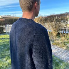 a man standing in the grass wearing a blue sweater