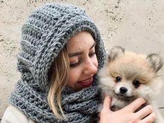 a woman is holding a small dog wearing a knitted hat and scarf over her head