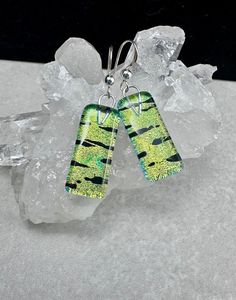 two green and black earrings sitting on top of ice