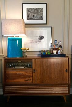 a wooden cabinet with a blue vase on top and a lamp next to it in a room