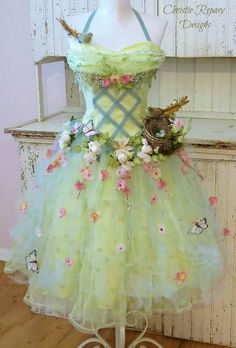 a green dress with flowers and birds on the front, sitting on a mannequin