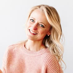 a woman with blonde hair and blue eyes smiles at the camera while wearing a pink sweater