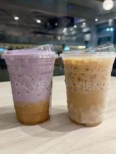 two iced coffees sitting on top of a table next to each other in plastic cups