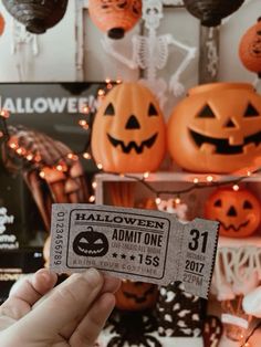 someone holding up a ticket for halloween with jack - o'- lanterns in the background