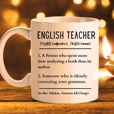 an english teacher coffee mug sitting on a table with a lit candle in the background