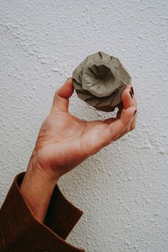 a hand holding a clay object in front of a white wall