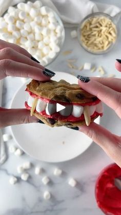 two hands holding a cookie with teeth and fangs on it, while the other hand holds a plate full of marshmallows