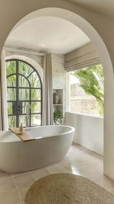 a large white bath tub sitting in a bathroom next to a window with an arched doorway