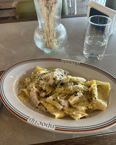 a white plate topped with pasta and meat covered in sauce next to a glass of water