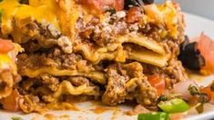 a white plate topped with lasagna covered in meat and cheese, tomatoes and green peppers