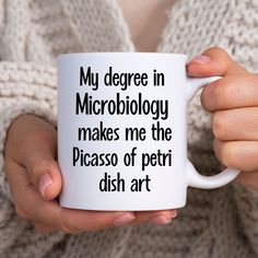 a person holding a coffee mug with words on it that read, my degree in microbiology makes me the picasso of petri dish art