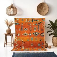 an orange and blue area rug in front of some potted plants on a white wall