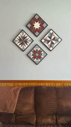 three quilts are hanging on the wall above a brown couch in a living room