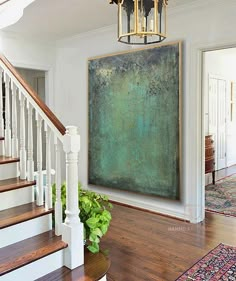 a large painting hanging on the wall next to a stair case and potted plant