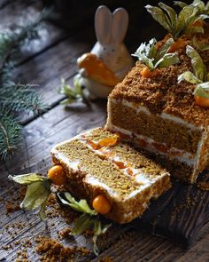 carrot cake with white frosting and sprinkles on wooden table next to bunny figurines