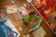 a woman is painting on the floor in front of many colorful art pieces and paintings