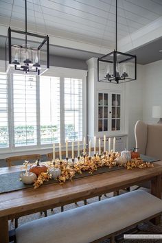 a dining room table with candles and fall decorations on it in front of the windows