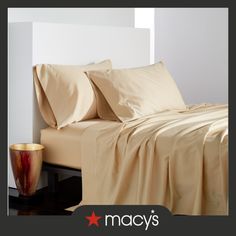 a bed with beige sheets and pillows on top of it next to a gold vase