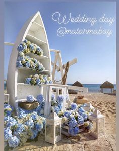 a wedding day on the beach with blue and white flowers in front of an old boat