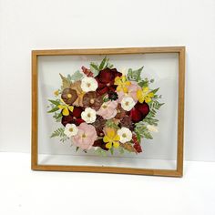 a wooden frame with flowers in it on a white wall next to a brown framed object