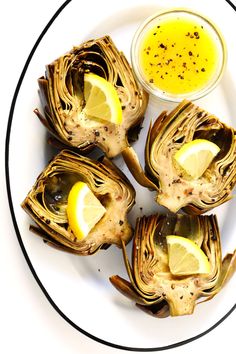 grilled artichokes with lemon and mustard on a white plate next to dipping sauce