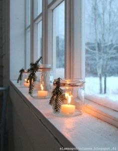 three jars with candles are sitting on a window sill in front of snow covered trees