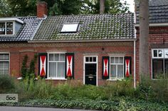 an old brick house with red and white striped shutters on the windows, in front of some trees