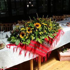 the table is set with sunflowers and greenery in red ribbon on it