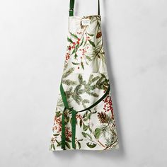 an apron hanging on the wall with holly and berries printed on it, along with green straps