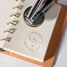 an open spiral bound notebook with pen and paper clippings on the cover, sitting on top of a white table